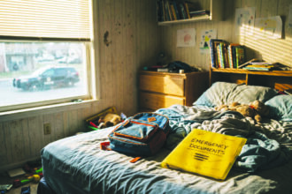 Habitación infantil vacía con una carpeta de documentos de emergencia sobre la cama, simbolizando a los niños separados de sus padres.