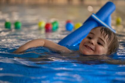 Niño feliz disfrutando sus clases de natación con un flotador azul, promoviendo seguridad en el agua y desarrollo temprano en la niñez
